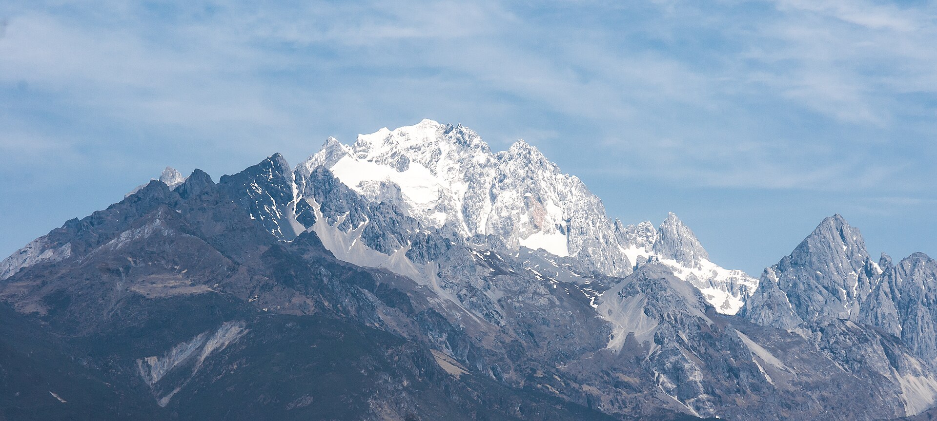 玉龙雪山群峰横亘于天边，雪线清晰，山脚下村舍炊烟，真实摄影